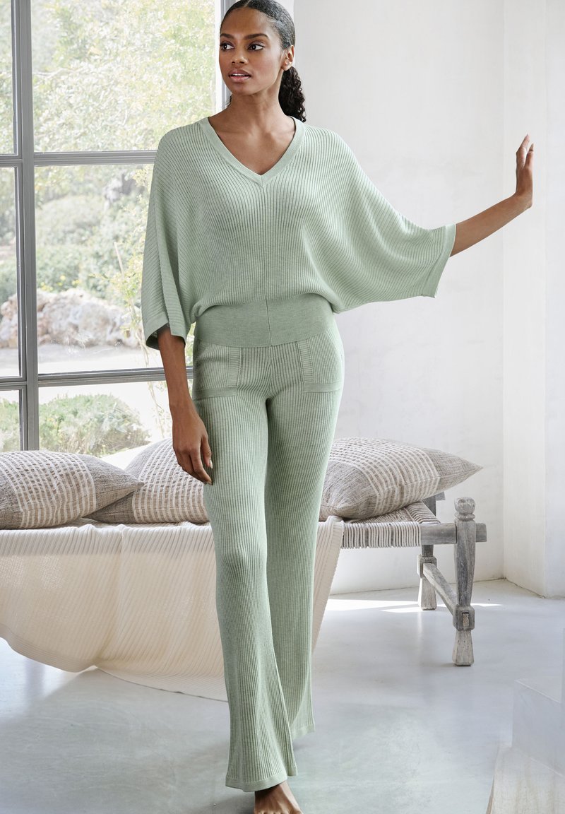 Lichtgroene gebreide co-ord-set met een V-hals top met brede mouwen en aansluitende, flared broeken met ribbeltextuur en subtiele naaddetails.