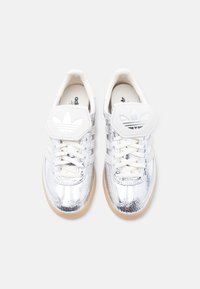 Paire de baskets basses métalliques argentées avec semelles en gomme, lacets blancs et languettes blanches ornées des logos trèfles d'Adidas, vue de dessus.