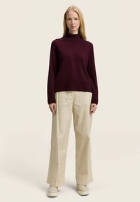 Bordo dolčevita uparena sa širokim svijetlo bež hlačama i svijetlom obućom, na neutralnoj pozadini.