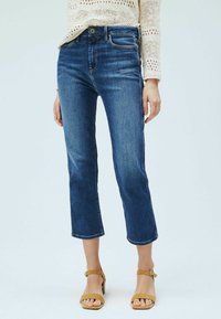 Mörkblå cropped jeans i denim, med en klassisk passform och subtila blekningar. Matchat med bruna remsandaler.