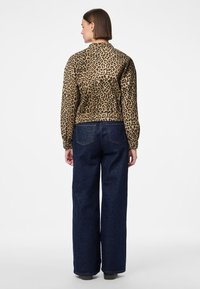 Jacka i leopardmönster med krage, långa ärmar och textilmaterial, kombinerad med löst sittande mörkblå jeans.