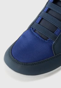 Donkerblauw sportschoen met een gestructureerde stoffen bovenkant en gladde leren accenten, platte veters en een ronde teenvorm.