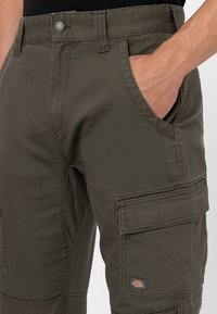 Olive green cargo pants made of sturdy fabric, featuring multiple pockets, reinforced stitching, and a button closure.