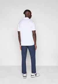 Λευκό πόλο μπλουζάκι με κοντά μανίκια, ναυτικά παντελόνια και γκρι αθλητικά παπούτσια. Το πόλο διαθέτει κλασικό γιακά και πλευρικές σχισμές για άνεση.