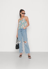 Top de alças com padrão floral em turquesa, combinado com jeans de perna larga em azul claro com efeito desgastado. Acessórios incluem óculos de sol pretos e uma bolsa preta.