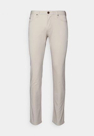 Pantaloni in cotone beige con taglio slim, dotati di un classico design a cinque tasche e un bottone marrone in vita. Texture liscia.