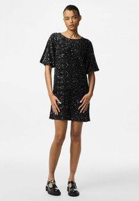 Melna sequins kleita ar īsām piedurknēm, noapaļotu kakla izgriezumu, līdz ceļiem garu apakšmalu, ar teksturētu virsmu un vaļīgu piegriezumu. Kopā ar melnajiem apaviem.