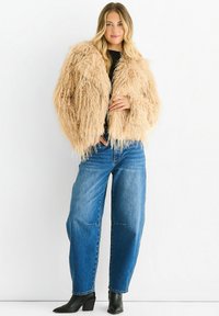 Fluffy beige faux fur jacket with a wide collar and loose fit, paired with high-waisted blue jeans and black ankle boots.