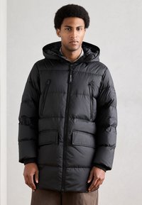 Casaco acolchoado preto com fecho dianteiro de correr, capuz e dois bolsos frontais. Apresenta padrão acolchoado horizontal e punhos elásticos.