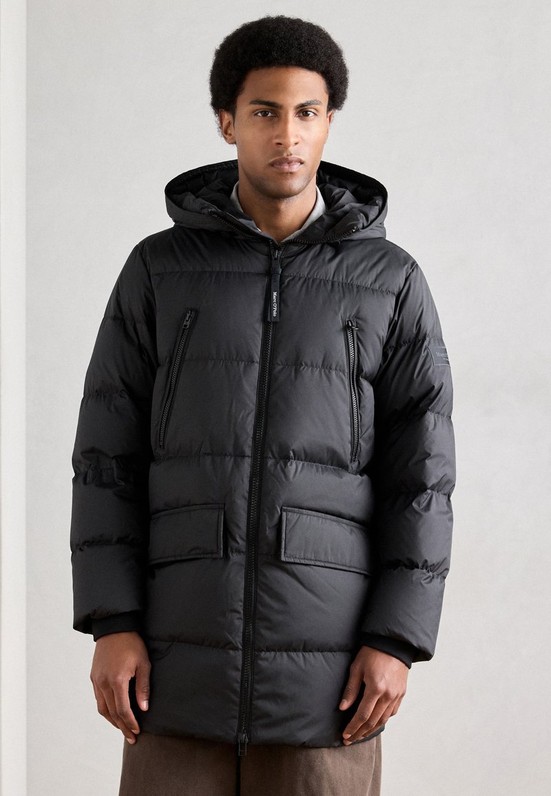 Casaco acolchoado preto com fecho dianteiro de correr, capuz e dois bolsos frontais. Apresenta padrão acolchoado horizontal e punhos elásticos.