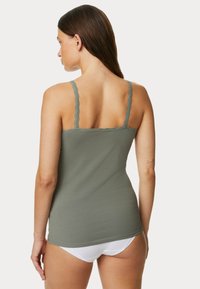 Oliwkowa kamizelka na ramiączkach z koronkowym wykończeniem. Posiada regulowane ramiączka i dopasowany fason, wykonana z miękkiego, elastycznego materiału bawełnianego.