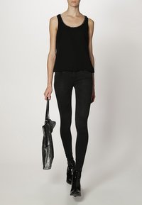 Haut sans manches noir avec un col scintillant, associé à un jean skinny noir et des bottines brillantes, tenant un sac à main métallique foncé.