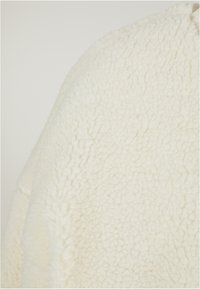 Tessuto in pile bianco con una superficie texturizzata e soffice. Morbido e spesso, presenta un motivo leggermente irregolare su tutto il materiale.