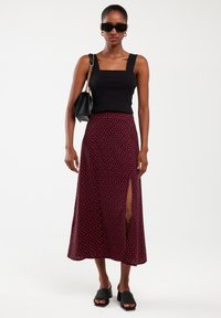 Black square-neck top, red patterned skirt with a side slit, and black open-toe heels. Accessories include black sunglasses and a shoulder bag.