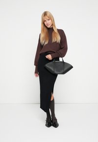 Brązowy prążkowany sweter, czarna prążkowana midi spódnica z bocznym rozcięciem, czarna usztywniana torebka oraz ciemnobrązowe skarpety do kolan zestawione z czarnymi butami.