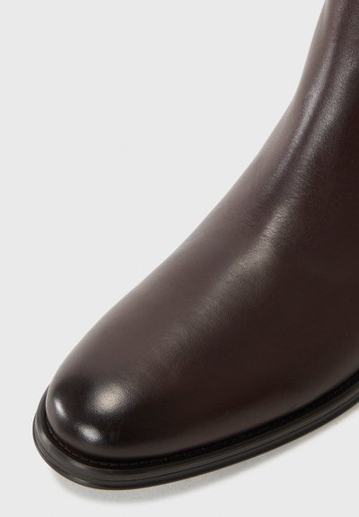 Bottine en cuir marron avec une texture lisse, bout rond et éclat subtil. Dispose d'une semelle noire et d'un design minimaliste.