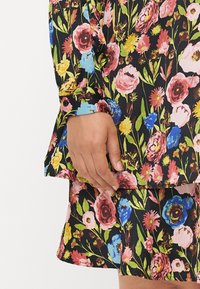 Floral top featuring a black background with multicolored flowers, long sleeves with buttons, and a layered hem. Textured fabric.