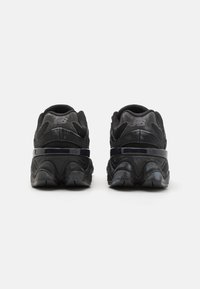 Chaussures de sport noires avec une tige en maille texturée, un col rembourré et une semelle extérieure en caoutchouc prononcée pour un support et une stabilité améliorés.