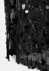 Tessuto nero con paillettes lucide e tonde cucite su uno sfondo di rete nera trasparente, creando una superficie strutturata e riflettente.