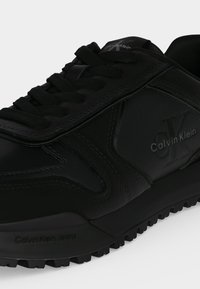 Baskets noires Calvin Klein avec lacets à l'avant, semelle texturée et logo embossé sur le côté et la languette.