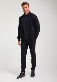 Ensemble de survêtement bleu marine comprenant une veste zippée et un pantalon assorti, confectionné en tissu doux. Présente un détail texturé sur le t-shirt et une accentuation sur la manche de la veste.