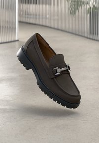 Brauner Lederloafer mit glatter Oberfläche, gepolstertem Kragen und dekorativer Metallspange. Verfügt über eine robuste schwarze Gummisohle.