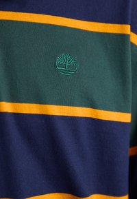 Cotton shirt featuring horizontal stripes in green, navy, and yellow, with a small green tree logo embroidered on the chest.