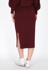 Bordeaux gebreide midi-rok met een zijsplit; gecombineerd met witte hoge sneakers. De textuur is glad en nauwsluitend, waardoor een slanke silhoeët benadrukt wordt.