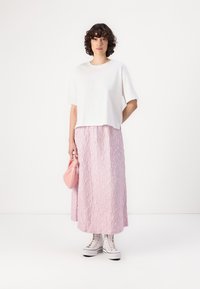 T-shirt blanc à manches courtes, jupe maxi en tissu texturé rose, baskets à plateforme blanches et pochette en tissu rose. Design de tenue simple et décontractée.