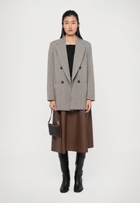 Blazer gris de cuadros de doble botonadura, camiseta negra, falda midi marrón, botas altas negras y llevando un pequeño bolso negro.