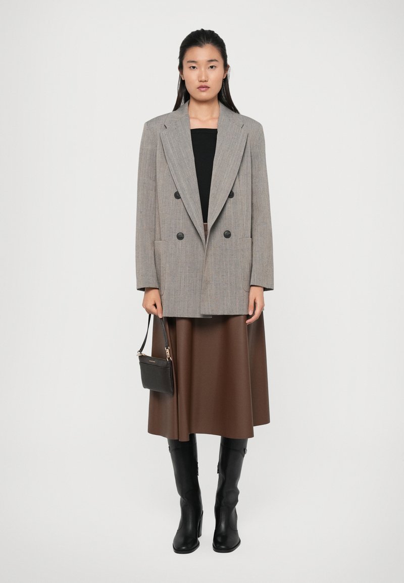 Blazer gris de cuadros de doble botonadura, camiseta negra, falda midi marrón, botas altas negras y llevando un pequeño bolso negro.