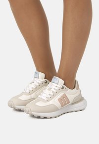 Beige Sportschuhe mit einer Kombination aus glatten und strukturierten Materialien, Schnürdesign, gepolsterten Sohlen und dezenten rosa Akzenten.