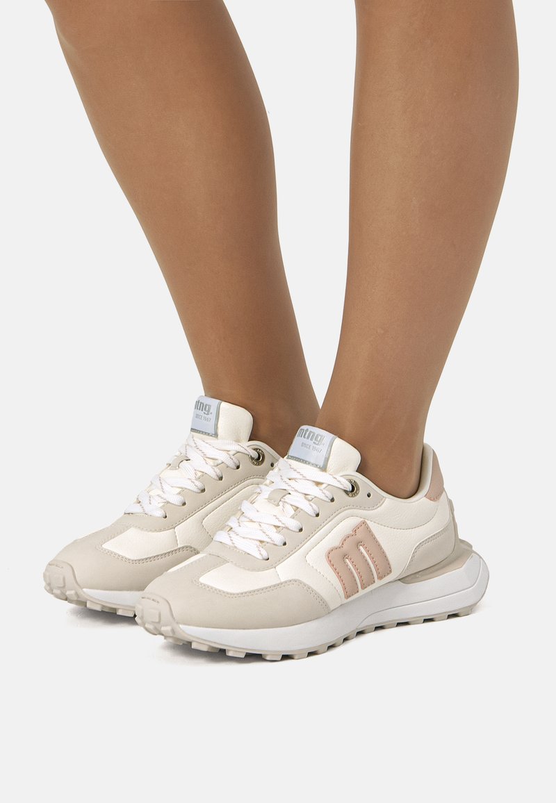Beige Sportschuhe mit einer Kombination aus glatten und strukturierten Materialien, Schnürdesign, gepolsterten Sohlen und dezenten rosa Akzenten.
