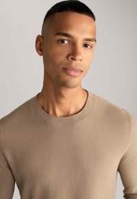 Pull en tricot beige avec un col rond, en tissu texturé et à coupe près du corps. La finition lisse améliore l'apparence générale simple.