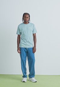 Lyseblå bomulds T-shirt med et lille logo, parret med løstsiddende blå denim jeans og hvide sneakers. Enkel, afslappet outfit.