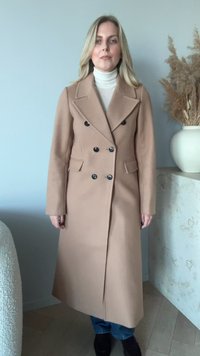 Dobbeltspent lang jakke i beige ullblanding med svarte knapper, spisse slag, sidelommer og rett snitt.