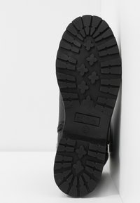 Semelle de botte noire avec des motifs de crampons profonds, comprenant des formes en croix, affichant la marque "s.Oliver" et la taille 37.