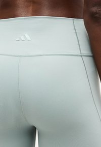 Gros plan sur une personne portant des leggings de sport taille haute bleu clair avec un petit logo Adidas sur la ceinture.