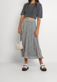 Grå kort t-shirt, blommig blå maxikjol med orangea och gula accenter, vita sandaler och en liten krämfärgad handväska med en silverkedja.