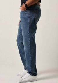 Jeans de mezclilla de color azul oscuro con un diseño de pierna recta, cinco bolsillos y un leve desgastado, combinados con zapatillas blancas.