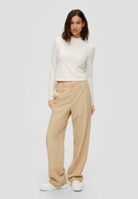 Witte textuur met lange mouwen crop top gecombineerd met beige met streepjes motief wijd-uitlopende broek en witte chunky sneakers. Lichte stof en moderne pasvorm.