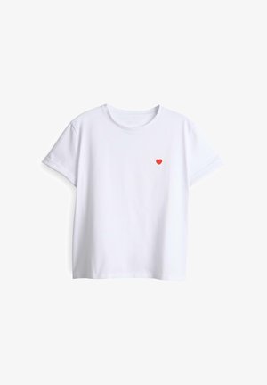 T-shirt blanc à manches courtes avec col rond et un petit cœur rouge brodé sur le côté gauche de la poitrine.