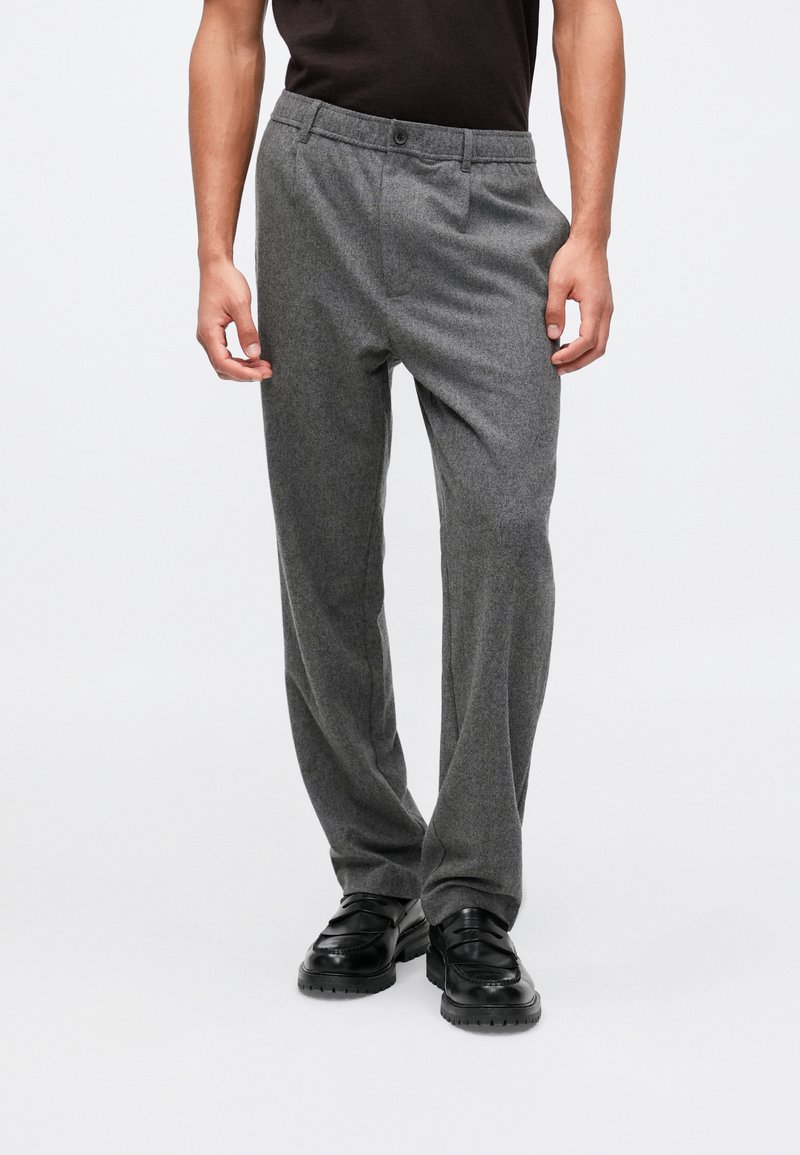 Sivi volneni hlače s ravnim krojem, sprednjim gumbom in stranskimi žepi. Ustrezajo črnimi mokasini.