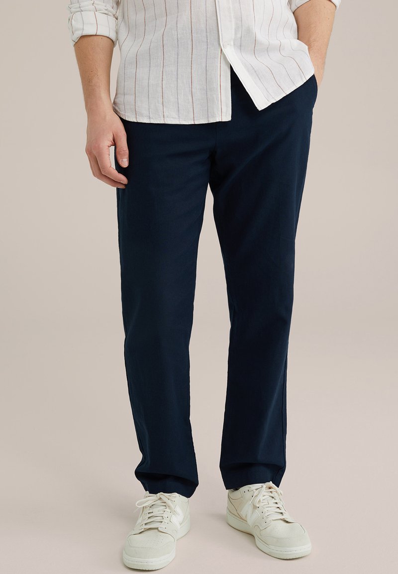 Mornarsko modri chinos hlače iz bombaža, s ravnim krojem in stranskimi žepi, v kombinaciji z belimi supergami za sproščen videz.