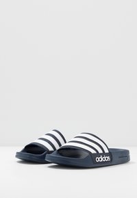 Marineblauwe slipppers met drie witte strepen over de bovenkant, met een gestructureerde voetbed en een logo aan de zijkant.