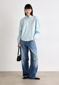 Lys blå skjorte med lange ermer, kombinert med slitte vide denimjeans. En svart håndv handbag og svarte leiligheter fullfører antrekket.