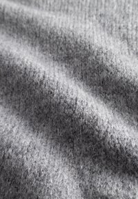 Tessuto grigio lavorato a maglia con una finitura morbida e testurizzata. Presenta un motivo a coste e una leggera lucentezza, che suggeriscono calore e comfort.