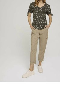 Top verde oliva con escote en V y patrón floral, mangas cortas con detalles de lazo, combinado con pantalones cargo beige y zapatillas blancas.