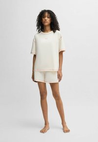 Krämfärgad kortärmad topp och shorts-set med rosa sömnadsdetaljer. Toppens design inkluderar en tryckt logotyp och en avslappnad passform, tillverkad av mjukt tyg.