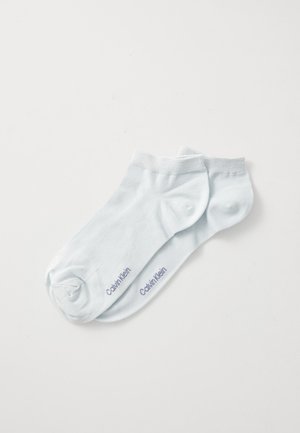 Šviesiai mėlynos kulkšninių kojinių pora su "Calvin Klein" logotipu, išspaudytu arti pirštų, ant balto fono.